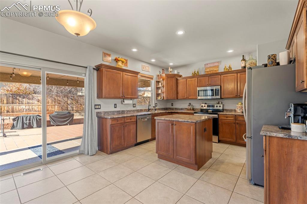 Image 9 of 41: Kitchen with brown cabinets, stainless steel appliances, light tile pattern