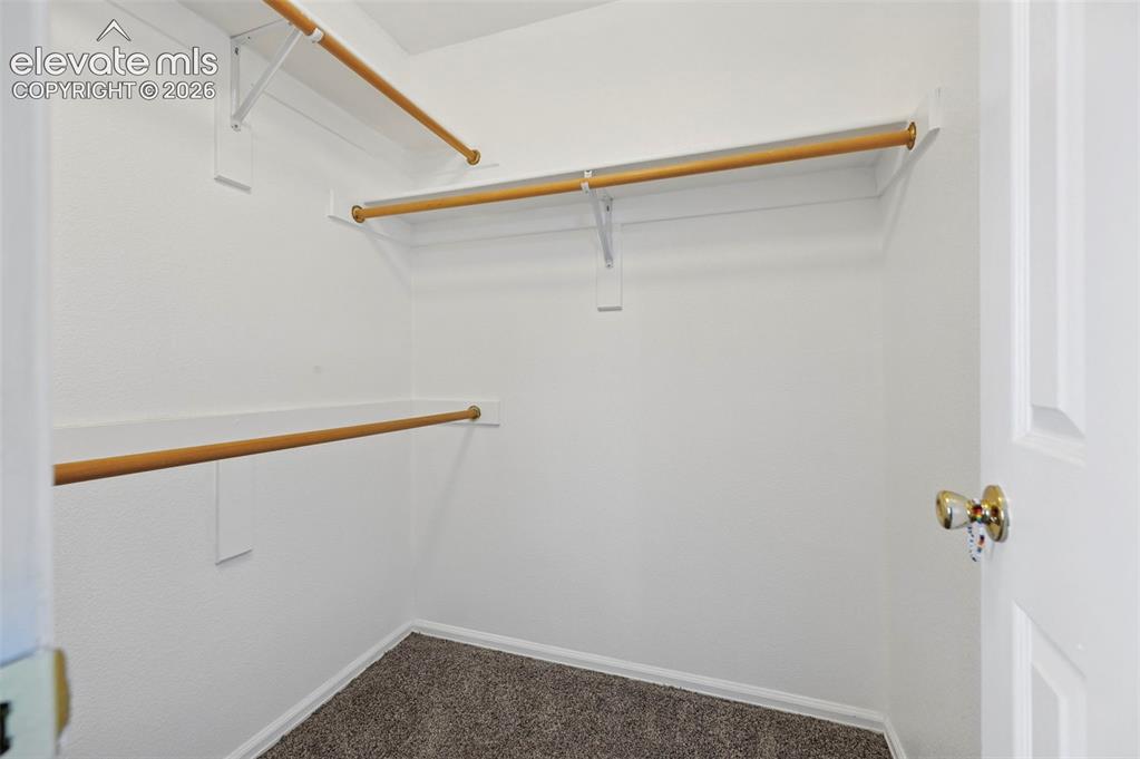 Image 22 of 27: Spacious walk-in closet featuring multiple wood-finish hanging rods, white