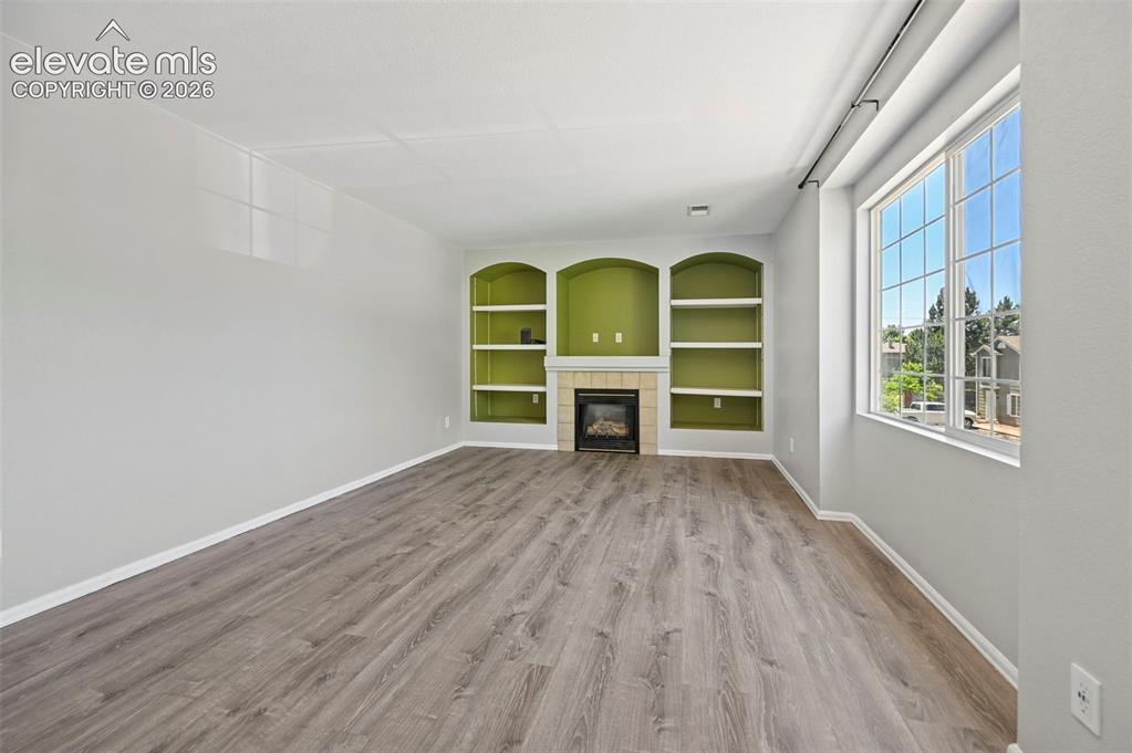 Image 8 of 27: Spacious living area featuring wood-finish flooring, a large window with gr