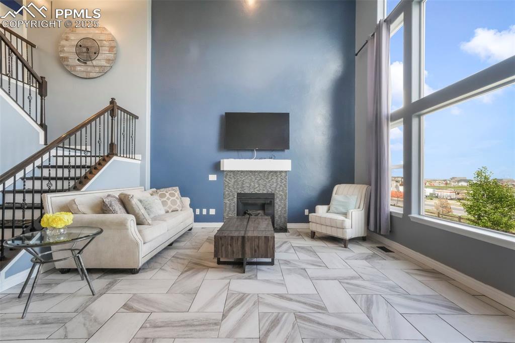 Image 16 of 50: Main level living room with fireplace, large windows and access to upper de