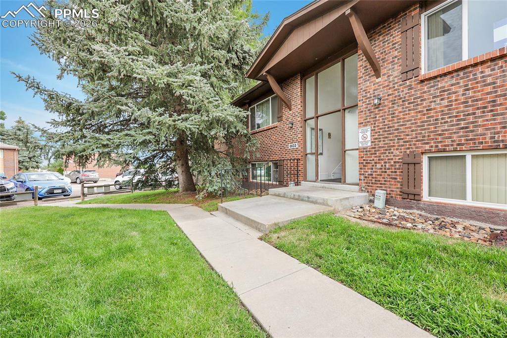 Image 14 of 27: View of exterior entry with brick siding and a lawn