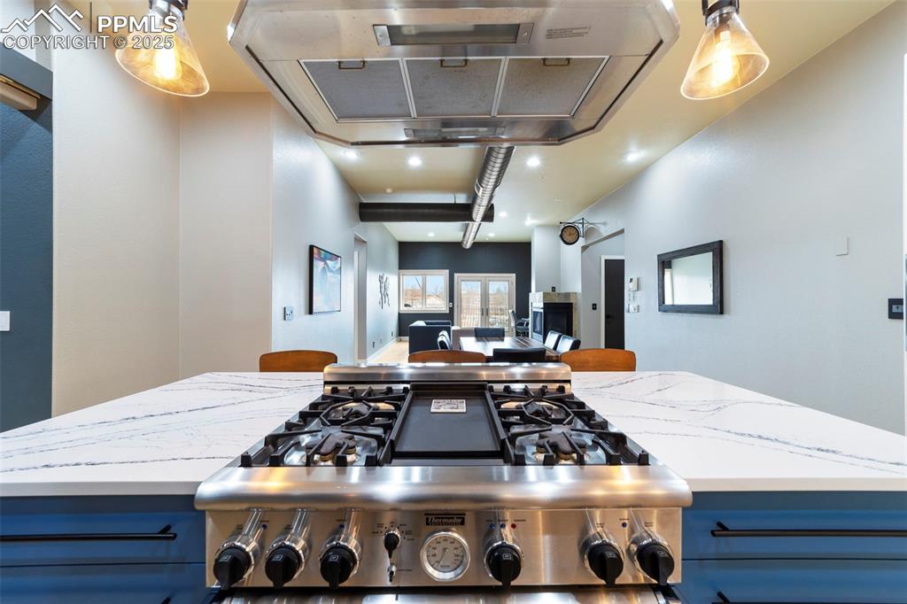 Image 10 of 40: Kitchen featuring exhaust hood, quartz countertops, pendant lighting, stain