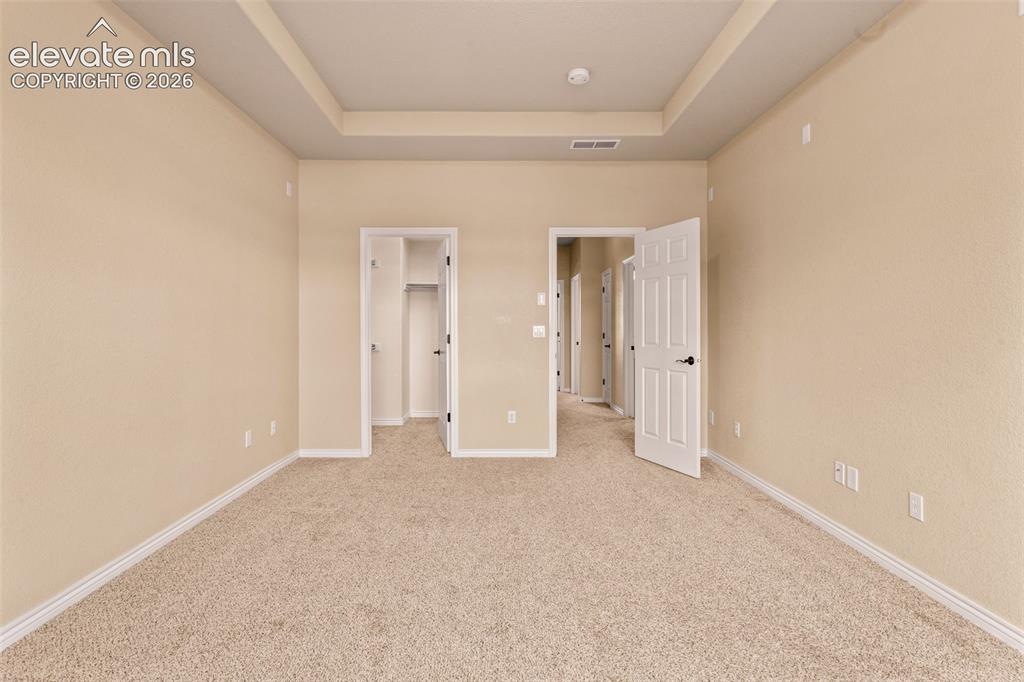 Image 14 of 26: Spacious room featuring neutral carpeting, tray ceiling, and light-toned wa