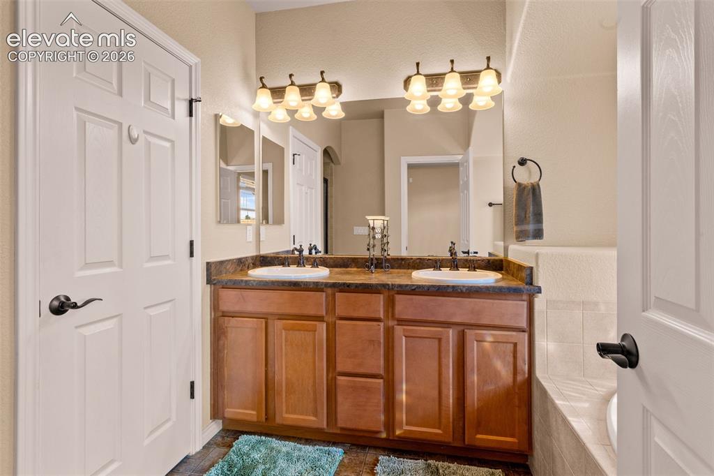 Image 17 of 26: Bathroom vanity featuring double sinks, a dark countertop, and wood-finish 
