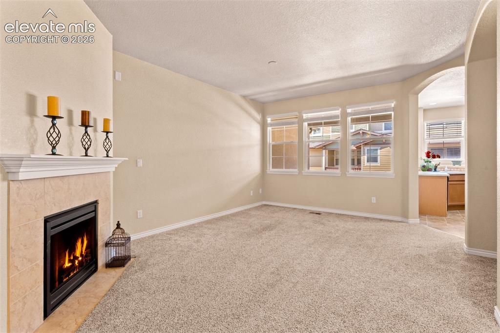 Image 26 of 26: Living area featuring a tiled fireplace with a mantel, three windows provid