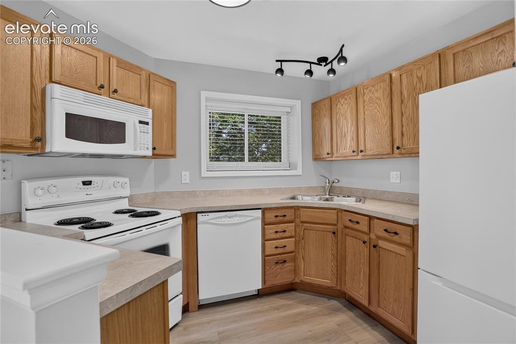 Image 21 of 44: Kitchen featuring wood-finish cabinetry, white appliances, light-toned coun