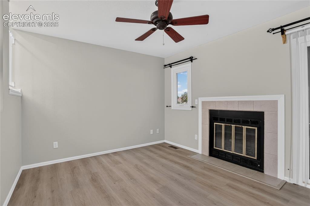 Image 7 of 44: Spacious room featuring wood-finish flooring, a ceiling fan, and a fireplac