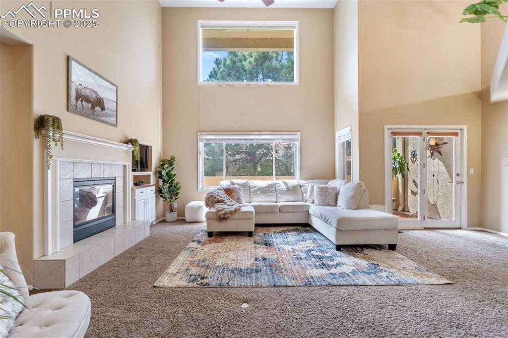 Image 12 of 50: Carpeted living area with a towering ceiling, a tiled fireplace, and a ceil