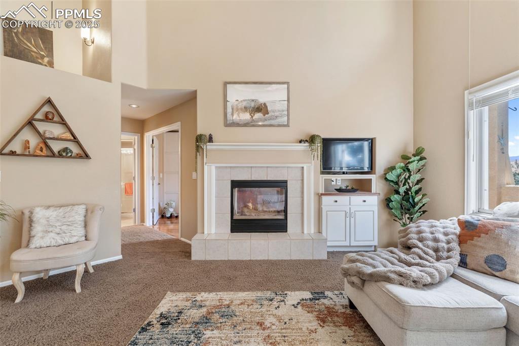 Image 15 of 50: Living area featuring a towering ceiling, a tile fireplace, and carpet floo