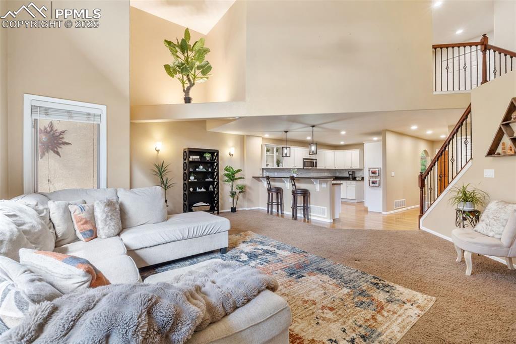 Image 16 of 50: Living room with light carpet, a high ceiling, and recessed lighting