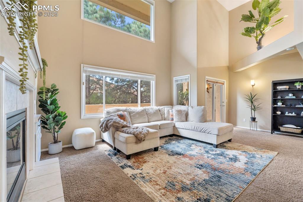 Image 17 of 50: Living room featuring a high ceiling, light carpet, and a fireplace with fl
