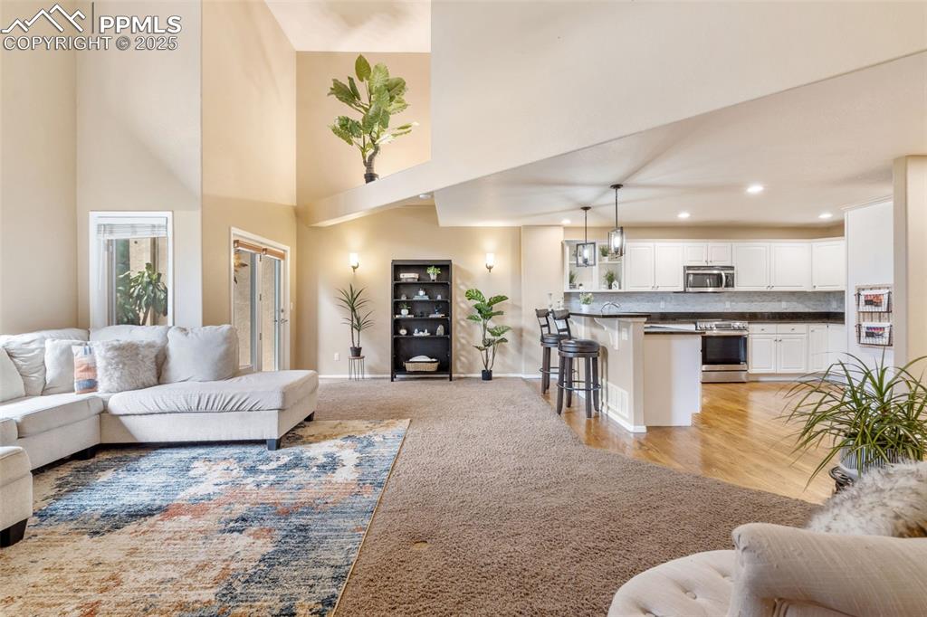 Image 18 of 50: Living room featuring a high ceiling, light colored carpet, recessed lighti