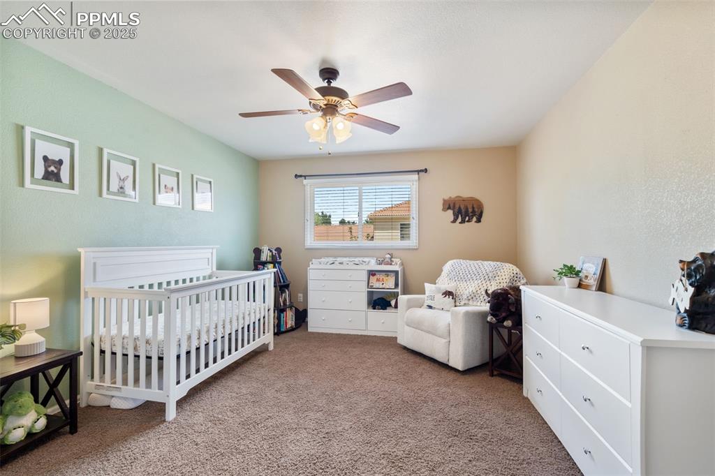 Image 20 of 50: Carpeted bedroom with a nursery area and ceiling fan