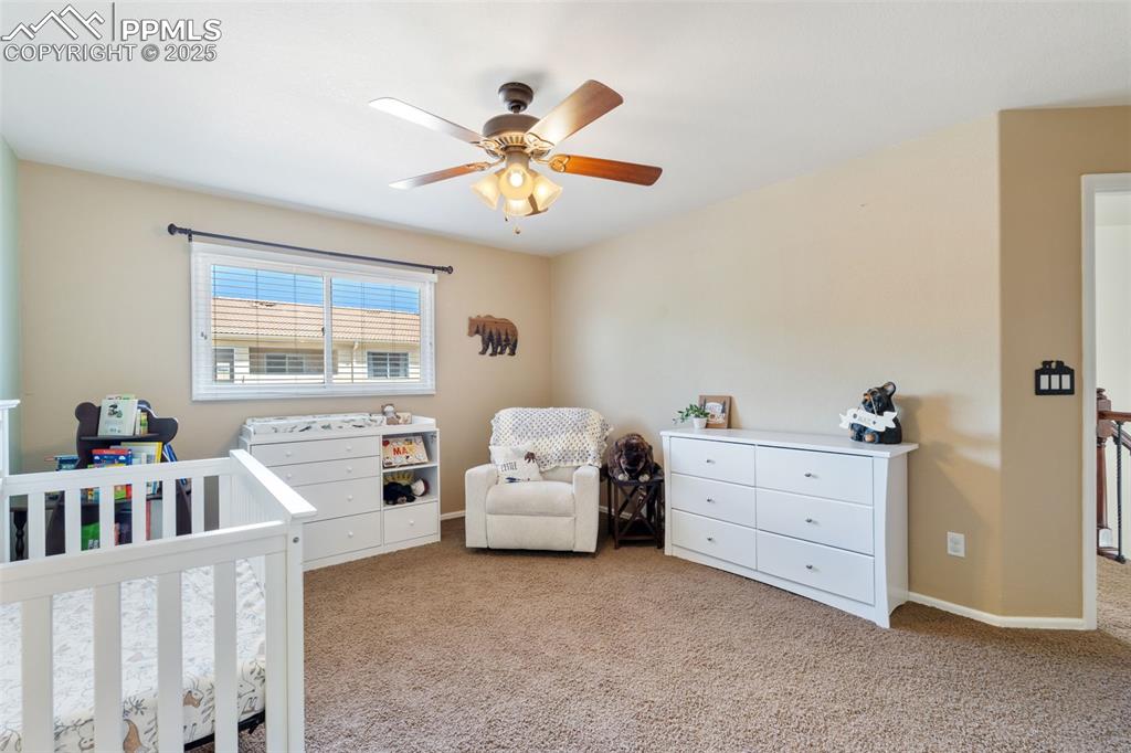 Image 21 of 50: Bedroom with a nursery area, light carpet, and ceiling fan