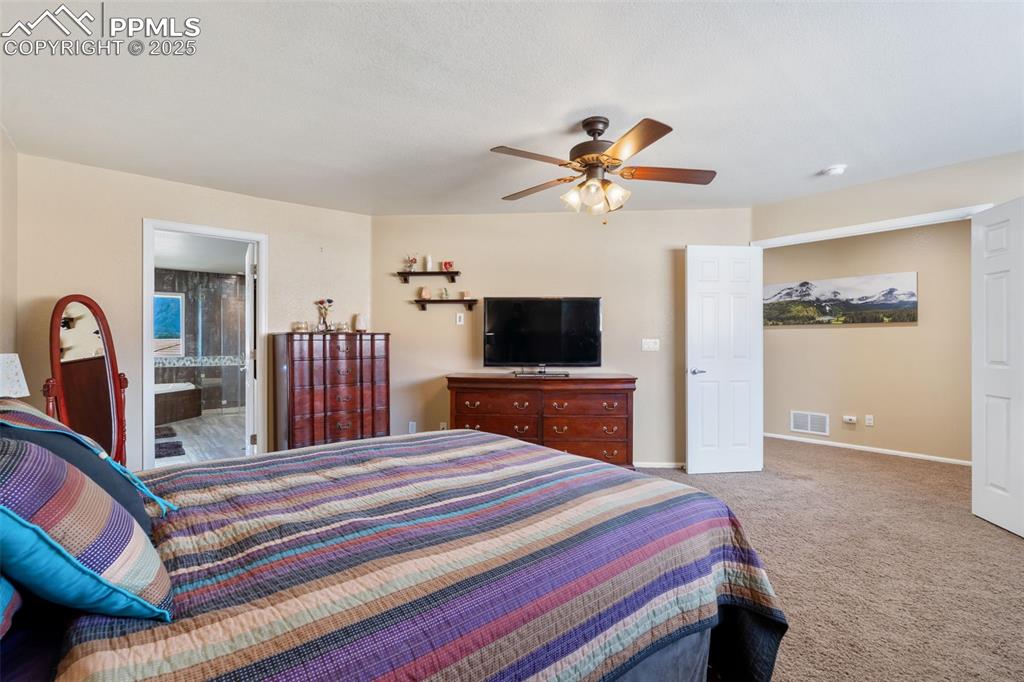 Image 25 of 50: Bedroom featuring light colored carpet, a ceiling fan, and connected bathro