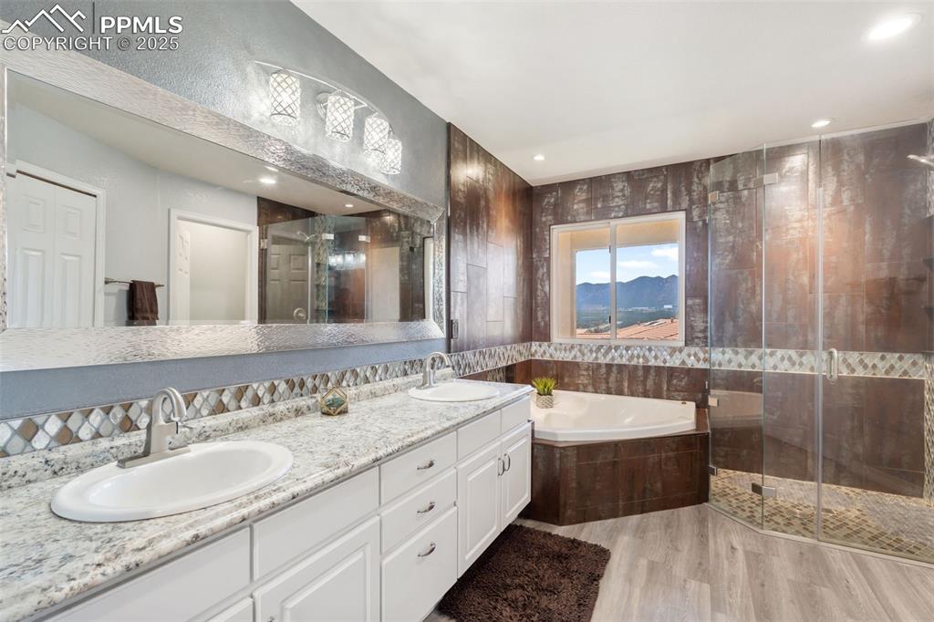 Image 26 of 50: Bathroom featuring a shower stall, a bath, double vanity, light wood-type f