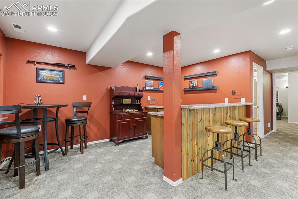Image 37 of 50: Indoor dry bar with a textured wall, light carpet, light stone counters, an