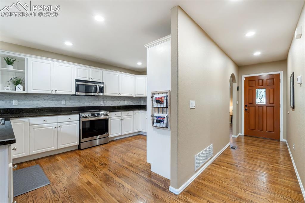 Image 6 of 50: Kitchen featuring white cabinetry, open shelves, decorative backsplash, sta