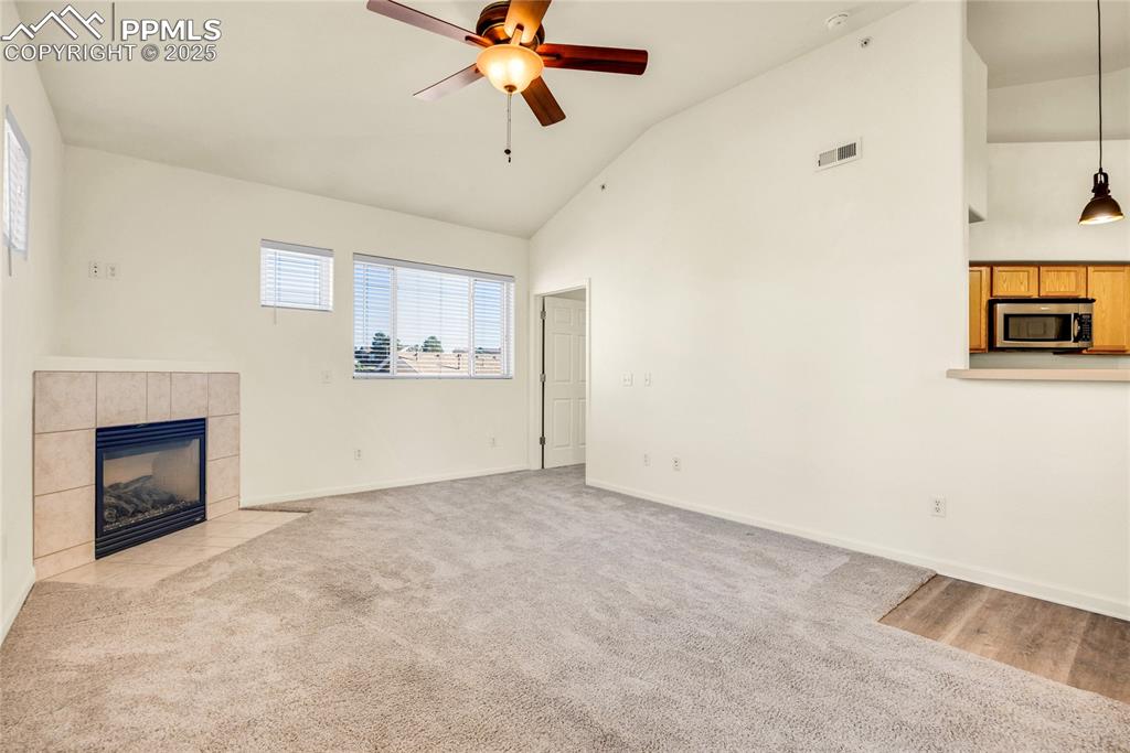 Image 14 of 37: Unfurnished living room with a tile fireplace, high vaulted ceiling, a ceil