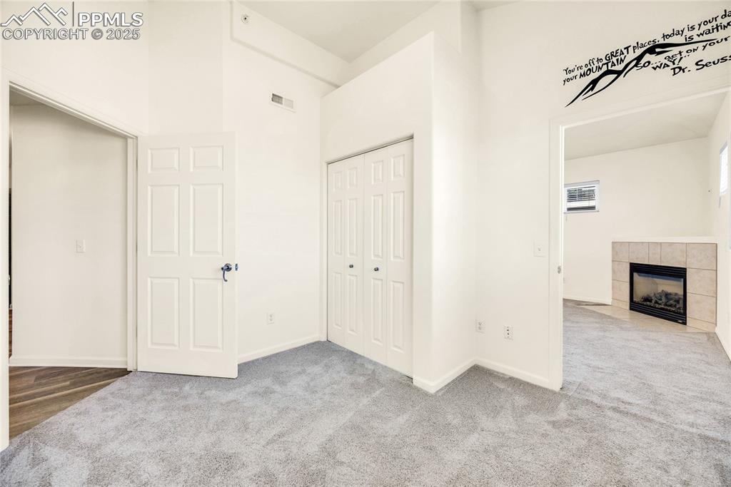 Image 23 of 37: Unfurnished bedroom featuring a towering ceiling, a tiled fireplace, carpet