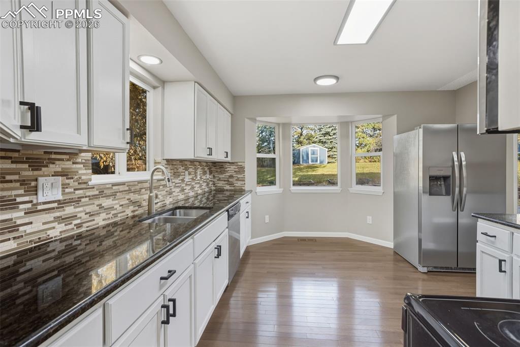 Image 16 of 36: Kitchen with stainless steel appliances, dark stone countertops, white cabi