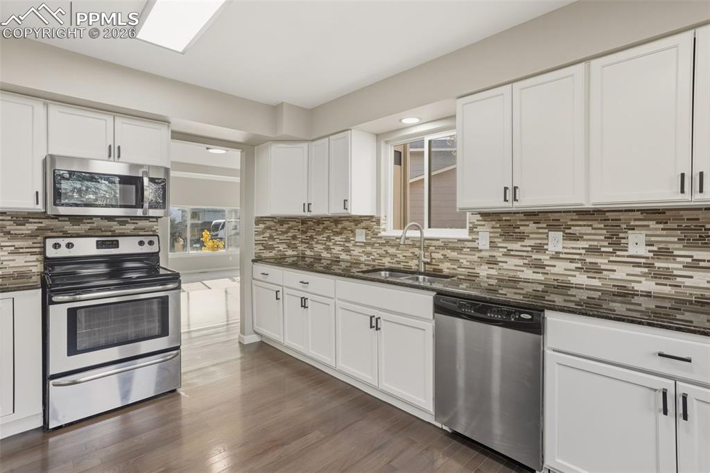 Image 3 of 36: Kitchen with stainless steel appliances, dark stone countertops, white cabi