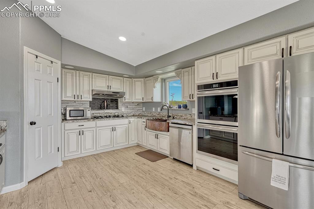 Image 19 of 50: Kitchen featuring stainless steel appliances, vaulted ceiling, light wood-s
