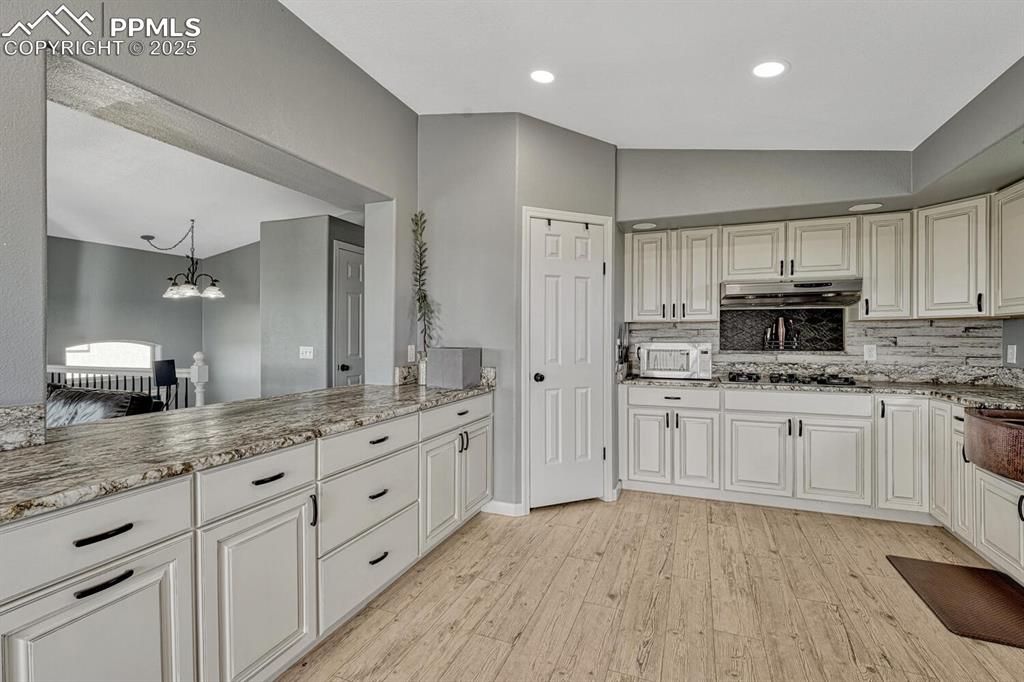 Image 22 of 50: Kitchen featuring light leathered granite countertops, backsplash, light wo