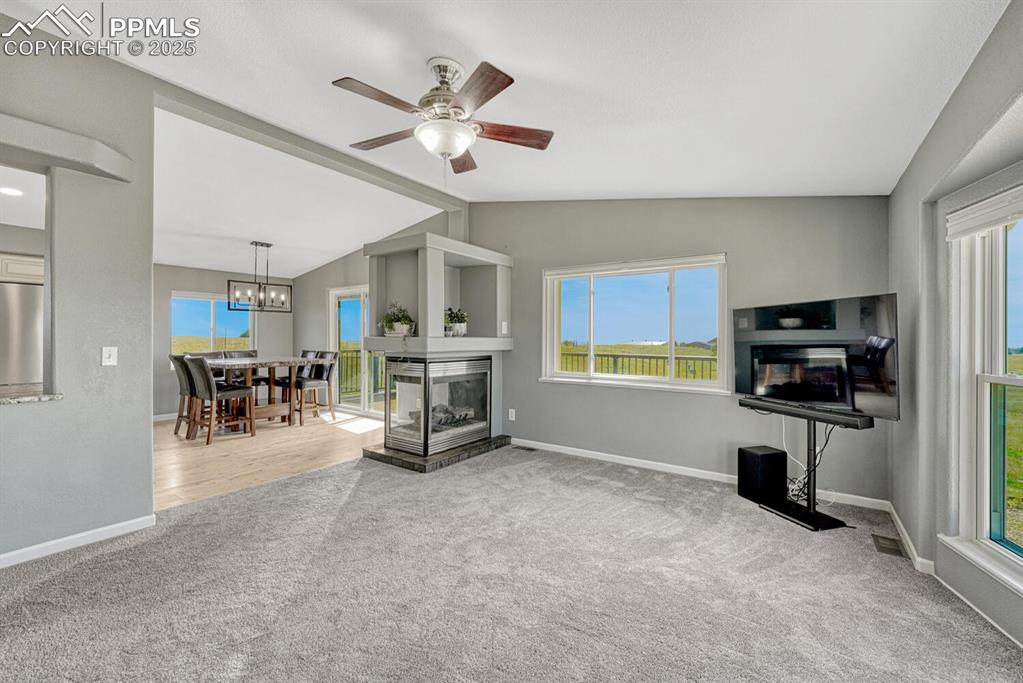 Image 34 of 50: Living room featuring a multi sided fireplace, light carpet, lofted ceiling