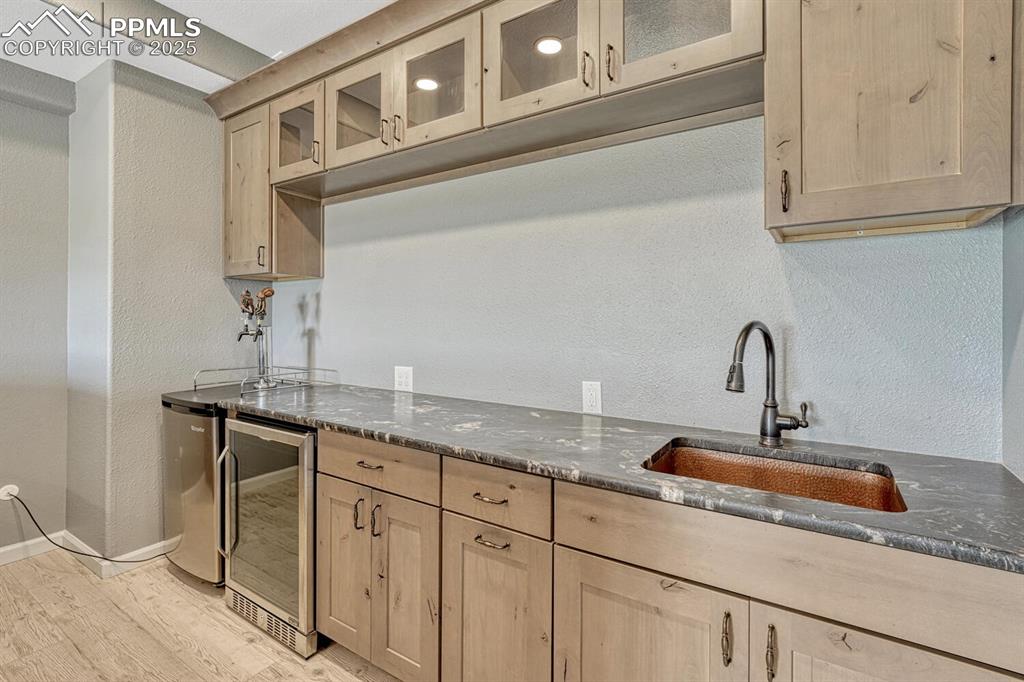 Image 41 of 50: Wet bar with glass insert cabinets, a textured wall, dark stone counters, l