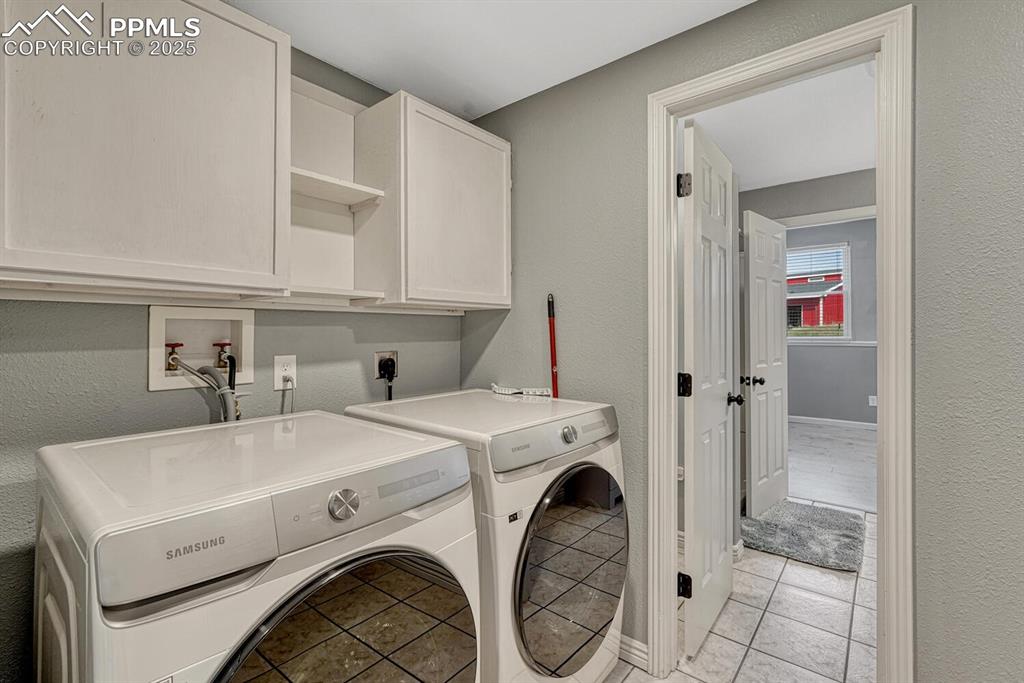 Image 49 of 50: Laundry area with a textured wall, light tile patterned floors, cabinet spa