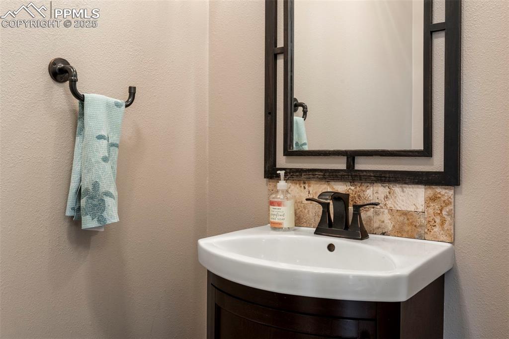 Image 12 of 46: Half bathroom with vanity, a textured wall, and decorative backsplash