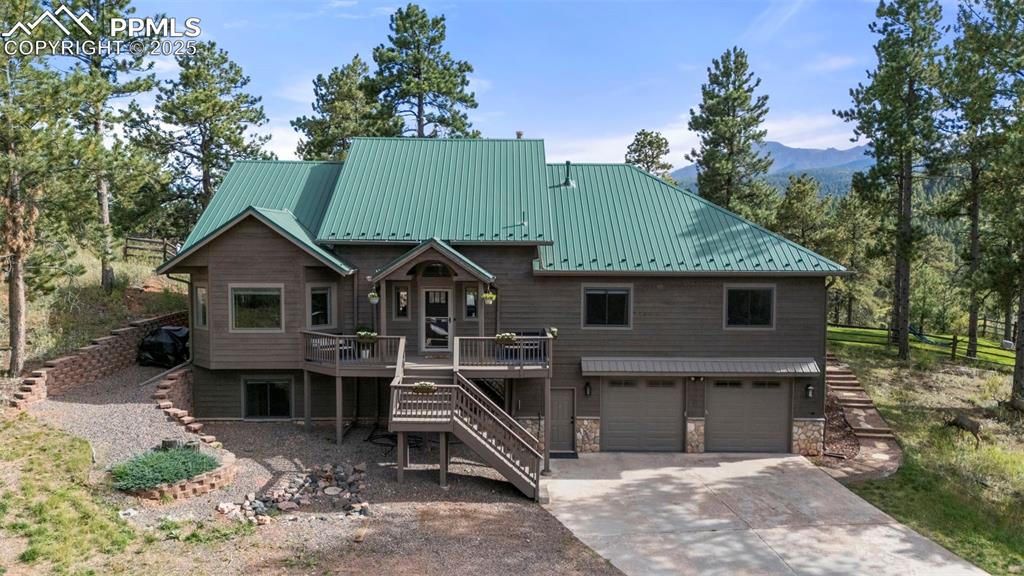 Image 39 of 46: Chalet / cabin with stairs, concrete driveway, a metal roof, an attached ga