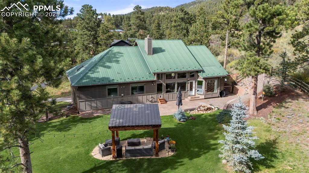 Image 45 of 46: Back of property featuring a patio area, a metal roof, a wooded view, outdo