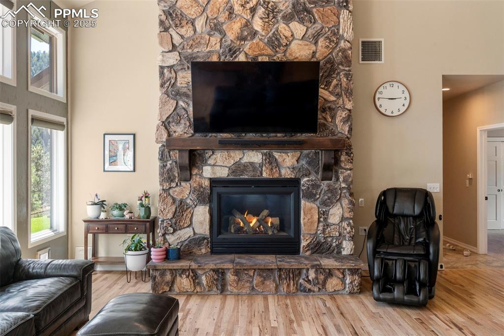 Image 5 of 46: Living room featuring a stone fireplace, wood finished floors, and a high c
