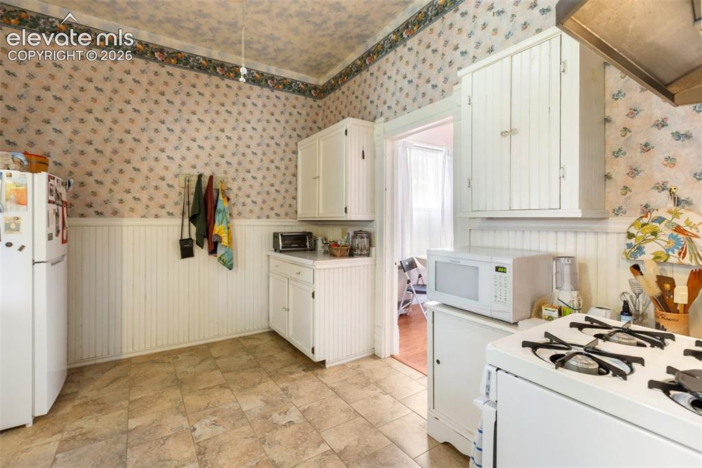 Image 15 of 29: Tile floors and to period wall paper create a bright and functional kitchen