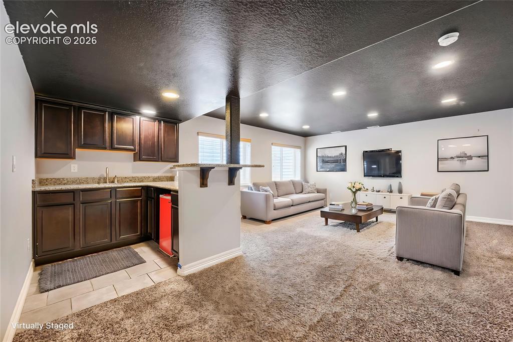 Image 28 of 41: Wet bar featuring dark wood-finish cabinetry, granite-style countertops, an