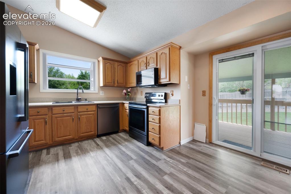 Image 10 of 50: Kitchen with stainless steel appliances, a sink, vaulted ceiling, light cou