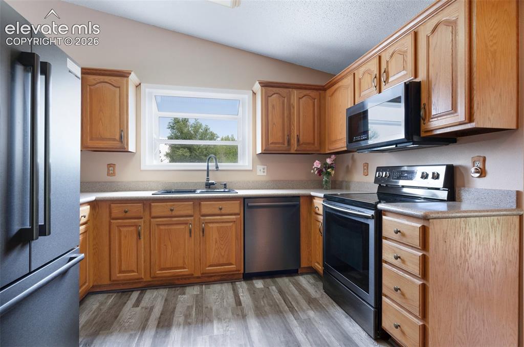 Image 11 of 50: Kitchen with stainless steel appliances, lofted ceiling, a sink, light coun