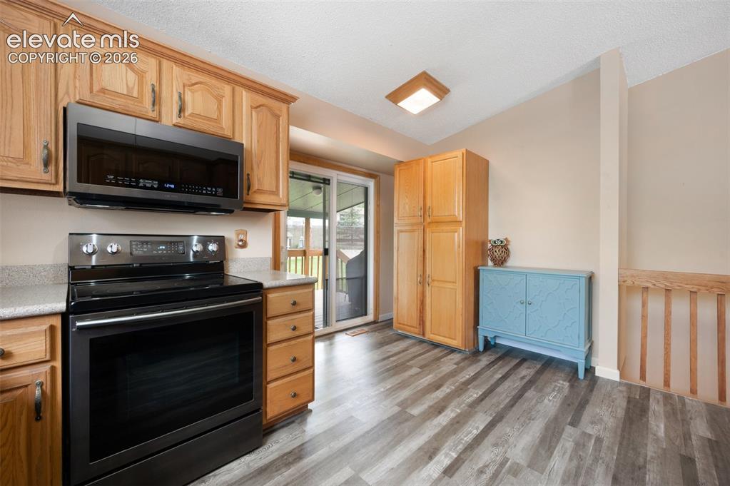 Image 15 of 50: Kitchen with black / electric stove, stainless steel microwave, light wood-
