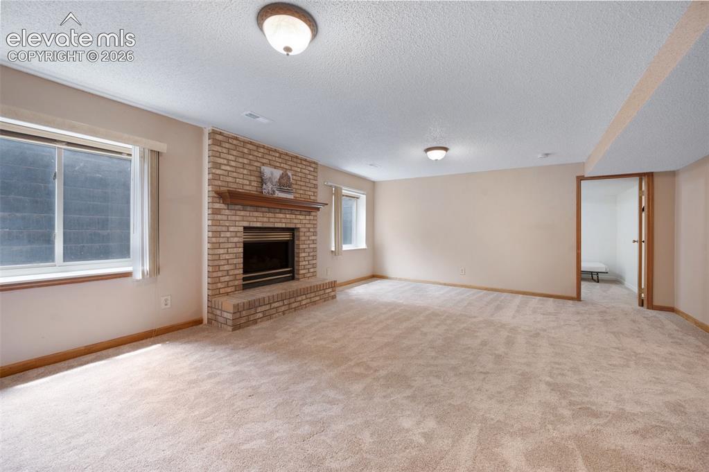 Image 28 of 50: Unfurnished living room with a textured ceiling, carpet flooring, a firepla