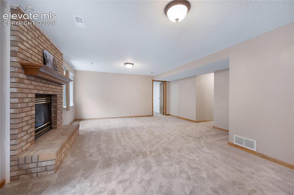 Image 29 of 50: Unfurnished living room featuring a fireplace, carpet, baseboards, and a te