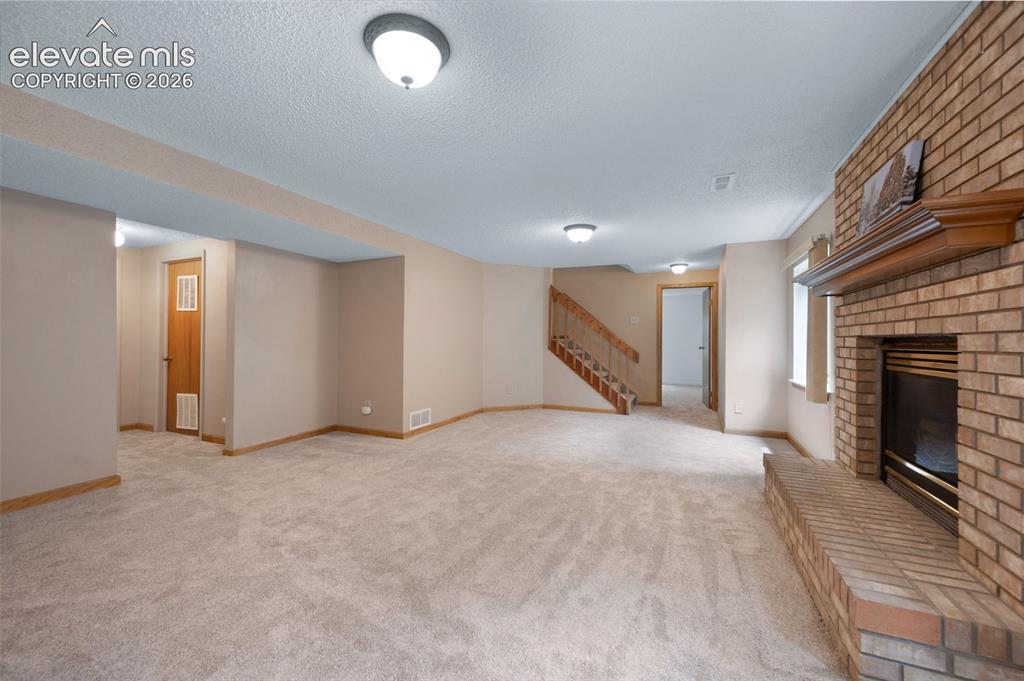 Image 30 of 50: Unfurnished living room with stairway, a brick fireplace, light carpet, a t