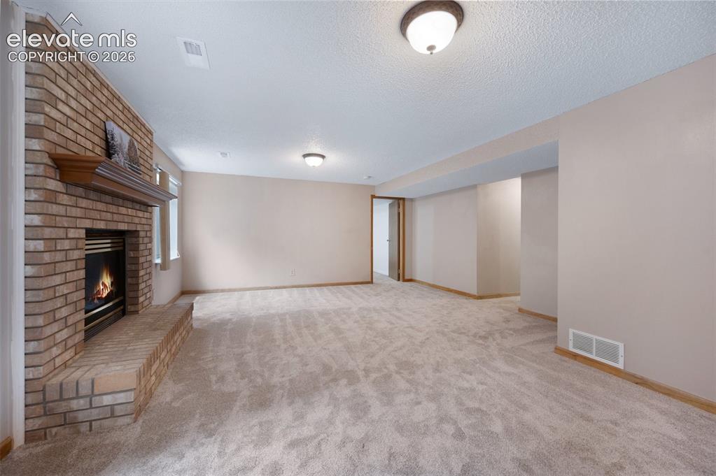 Image 33 of 50: Unfurnished living room featuring carpet, a brick fireplace, baseboards, an