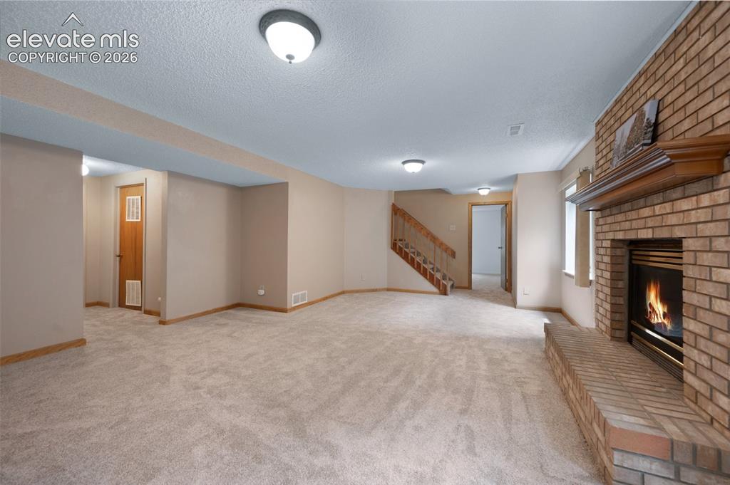 Image 34 of 50: Unfurnished living room with a fireplace, stairway, a textured ceiling, lig