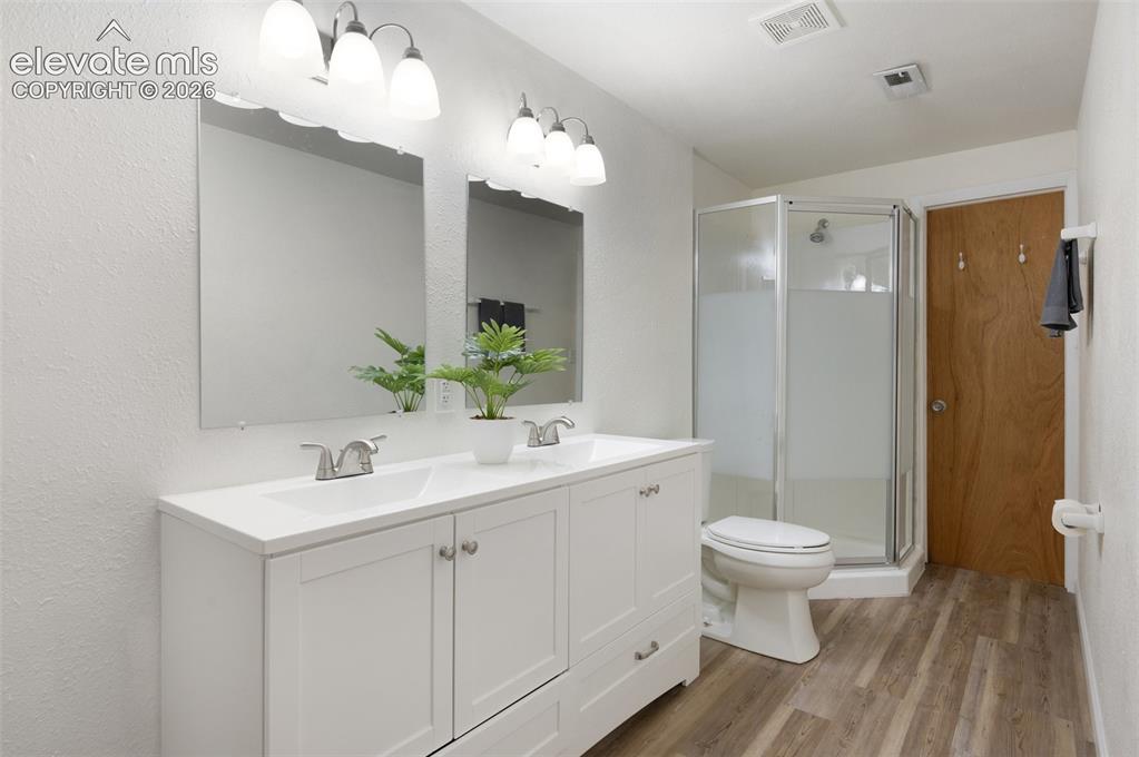 Image 40 of 50: Full bath with wood finished floors, a stall shower, toilet, and double van