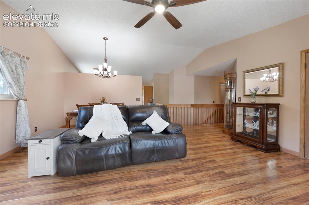 Image 6 of 50: Living area featuring vaulted ceiling, ceiling fan, a chandelier, light woo