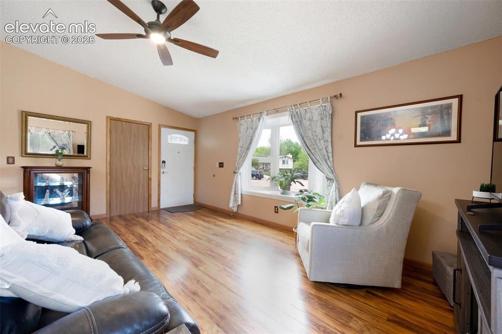 Image 7 of 50: Living area featuring light wood-style floors, vaulted ceiling, ceiling fan