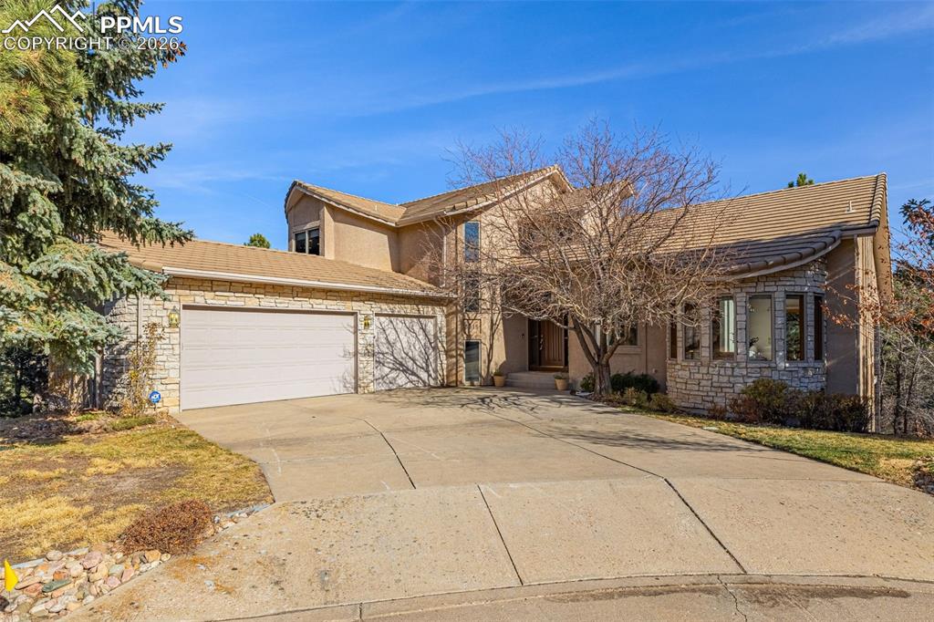 Image 2 of 47: Traditional-style house featuring a garage, stone siding, concrete driveway
