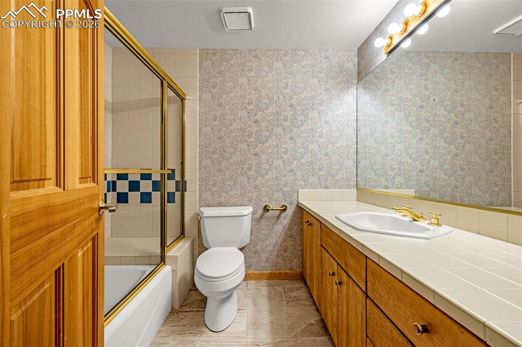 Image 40 of 47: Bathroom with bath / shower combo with glass door, vanity, a textured ceili